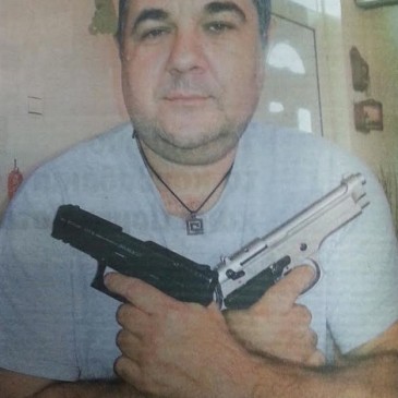Γιώργος Ρουπακιάς με δύο πιστόλια χιαστί σαν Τζέημς Μποντ και κρεμαστό κόσμημα στο λαιμό με μαίανδρο ΧΑ, RealNews, 05/10/2014.
