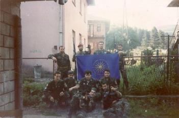 Βλασένιτσα, 1995, άνδρες της ΕΕΦ με την σημαία της Βεργίνας. Διακρίνεται το στέλεχος της Χρυσής Αυγής Τζανόπουλος Σπύρος (λοχίας της ΕΕΦ) και οι Ζαβιτσάνος Δημήτριος (αρχιλοχίας της ΕΕΦ), Kαλτσούνης Κωνσταντίνος, Αννα Φλορίν, Μήτκος Αντώνιος (διοικητής της ΕΕΦ), Βασιλειάδης Τρύφων (υποδιοικητής της ΕΕΦ), Σχιζάς Βασίλης, Κυριακίδης Κ., Λυμπερίδης Γ. και Δημουλάς Xαράλαμπος. Το σήμα με τα τρία δάχτυλα που κάνει στην κάμερα ο Ζαβιτσάνος είναι το σερβικό εθνικιστικό σήμα του νέου σερβικού μεγαλοϊδεατισμού που έκαναν όλοι οι Σέρβοι από τότε που ξεκίνησε η διάλυση της Γιουγκοσλαβίας και σε όλη τη διάρκεια του πολέμου. Και ακόμα το κάνουν.