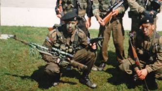 Με στολή παραλλαγής και τουφέκι σνάιπερ με διόπτρα στο ένα χέρι και κάποιο αυτόματο όπλο στο άλλο χέρι: Ελευθέριος Σπουργίτης, διωγμένο μέλος της ΕΕΦ.