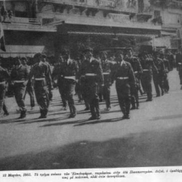 Οδός Πανεπιστημίου, 23 Μαρτίου 1963. Το τμήμα Νέων των Ελπιδοφόρων παρελαύνει με πλήρεις στολές, διάσημα, αμφιμασχάλια και εξαρτύσεις, κατόπιν εγκυκλίου του Υπουργείου Παιδείας και του υπουργού Γεωργίου Ράλλη. Ο ομαδάρχης τους με πολιτικά δίπλα στον αστυφύλακα. Στην ίδια παρέλαση μπροστά στον Αγνωστο Στρατιώτη, συμμετείχε και άλλο άγημα, των λεγομένων 'Μελανοχιτώνων', επίσης με επίσημη άδεια απ' το υπουργείο. Η φωτογραφία από το περιοδικό 'Δρόμοι της Ειρήνης'. Την ίδια στιγμή, αντιπροσωπεία σπουδαστών που προσπάθησε να καταθέσει στεφάνι στο άγαλμα του Ρήγα Φεραίου στα Προπύλαια δέχτηκε επίθεση από αστυφύλακες. Ποδοπάτησαν το στεφάνι και ακολούθησαν τραμπουκισμοί και συλλήψεις.